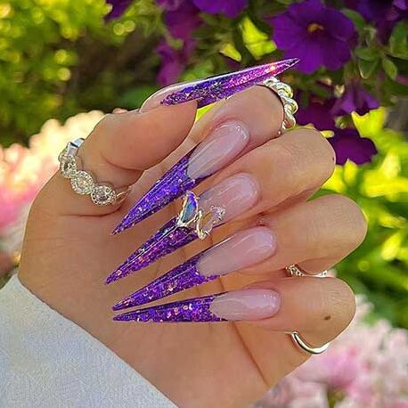 Long stiletto shaped purple glitter French tip nails with a butterfly rhinestone