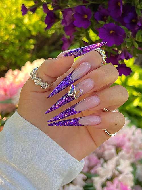 Long stiletto shaped purple glitter French tip nails with a butterfly rhinestone