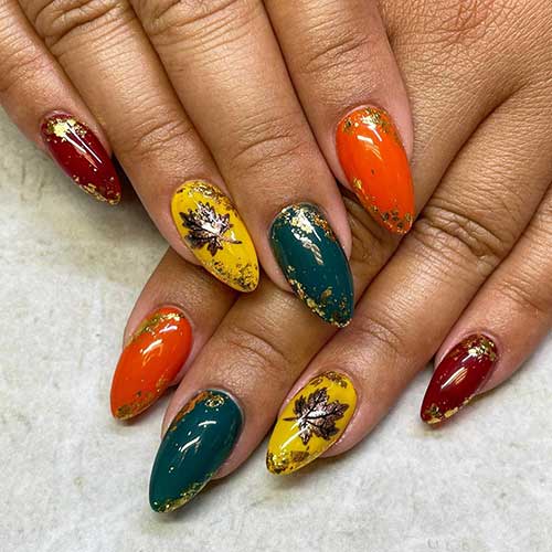 Almond fall nails with different autumnal colors reddish brown, burnt yellow, orange, and dusty blue adorned with gold foil patches.