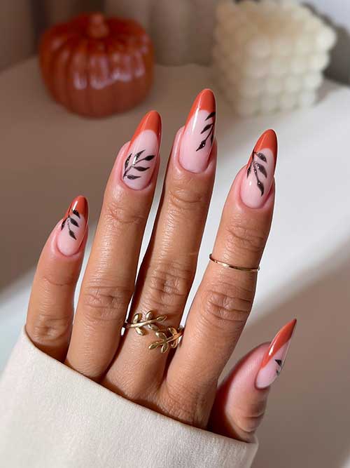 Burnt orange French nails on a nude base, adorned with black leaves and subtle glitter accents for a stylish autumn look.