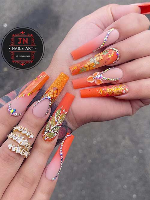 Cute long coffin-shaped orange autumn nails featuring leaf and floral designs, silver rhinestones, and pumpkin spice glitter.