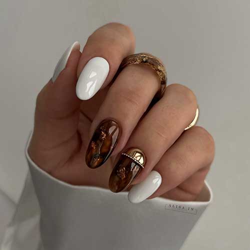 Elegant white nails with two accent nails: brown marble effects, gold foil, and one with gold chrome and rhinestones.