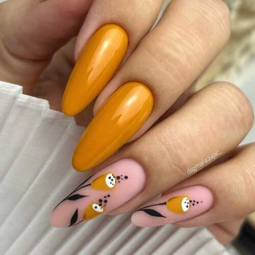 Long almond-shaped glossy burnt yellow nails, leaf nail art, and dainty flowers on two accent nude pink nails