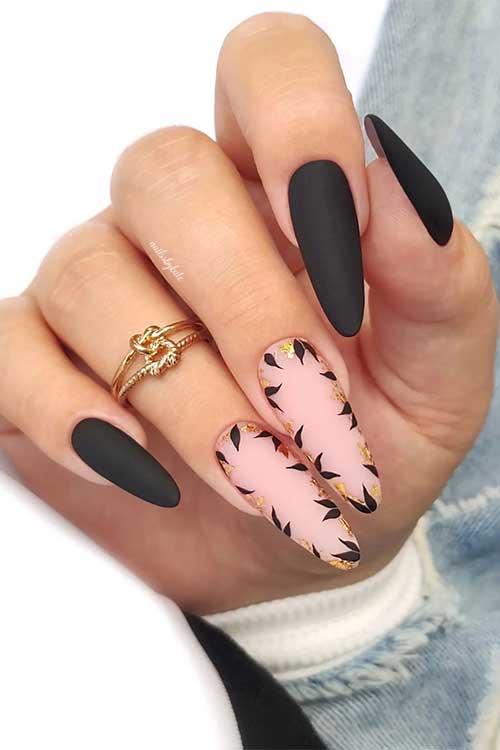 Long almond shaped matte black nails and intricate leaf nail art enhanced with gold foil flakes