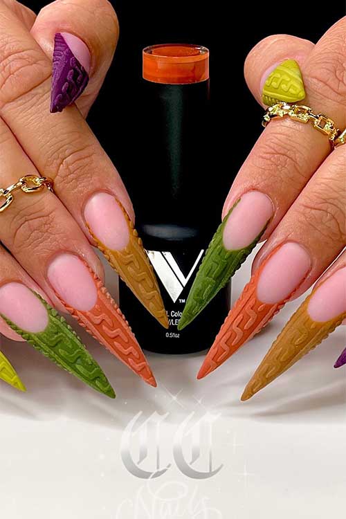 Long stiletto multicolored French Sweater Nails with different green, brown, and purple nail colors.