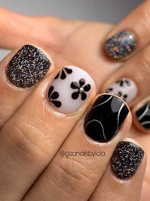 Short black nails with glitter on two accent nails, silver swirl art on another, and a milky white nail with black flowers.