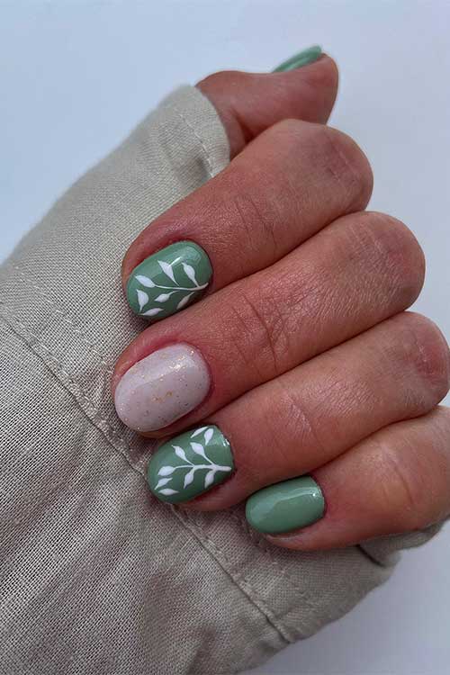 Short light green nails with white leaf nail art and a nude pink accent nail adorned with gold glitter