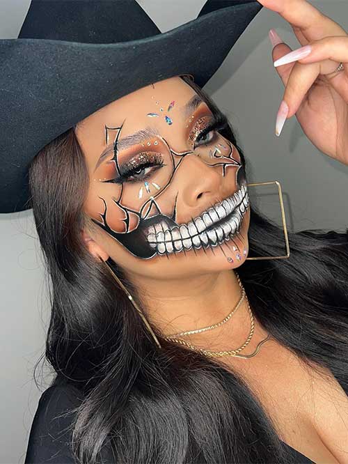 Black and white skull makeup features teeth and cracks on the face with pretty smoky brown eyes and glittery eyelids