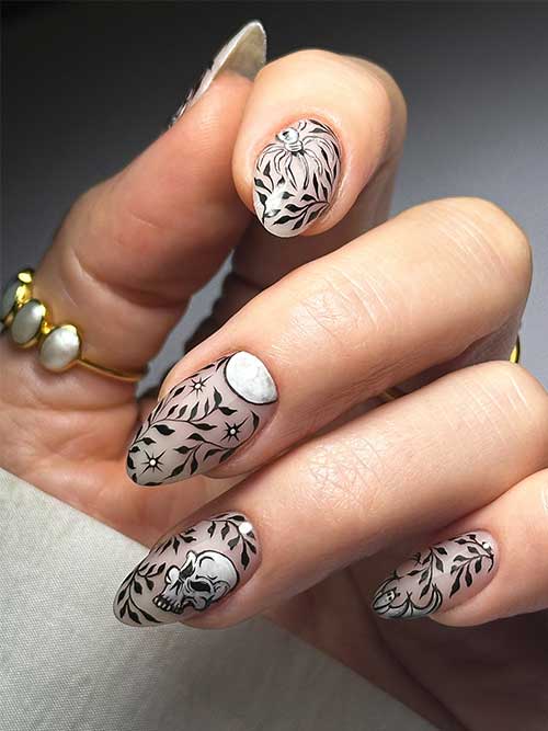 Creative Halloween nails with black leaf art and white Halloween motifs on a nude base, showcasing festive elegance.