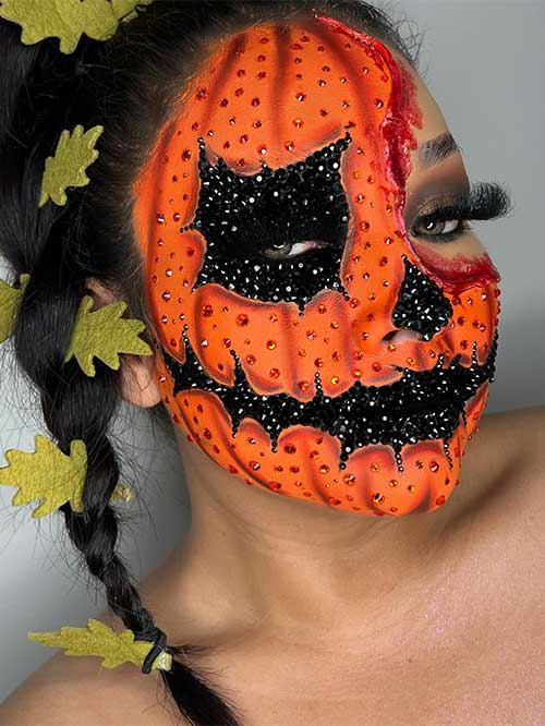 Orange rhinestone pumpkin Halloween makeup covers all face except the left upper corner which shows a bloody outline