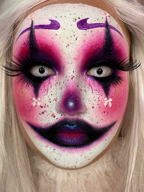 Spooky clown makeup featuring white face paint, dark violet lips, red eyeshadow around the eyes and cheeks, and dramatic eyebrows.