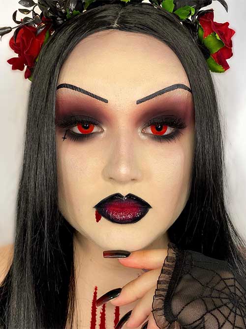 Spooky vampire Halloween makeup look with red contact eyes, Smokey eyes, and red and black vampy lips with a blood drip