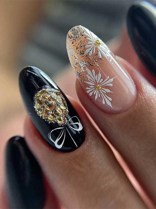 Black Christmas nails with a gold glittery gift ball and a nude accent nail adorned with white snowflakes and gold glitter