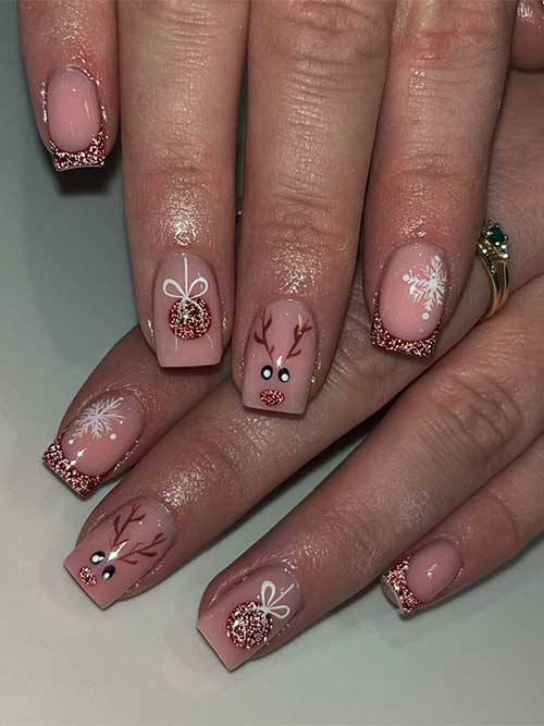Rose gold glitter Christmas nails feature French tips and a nude accent nail adorned with a reindeer face and a gift ball