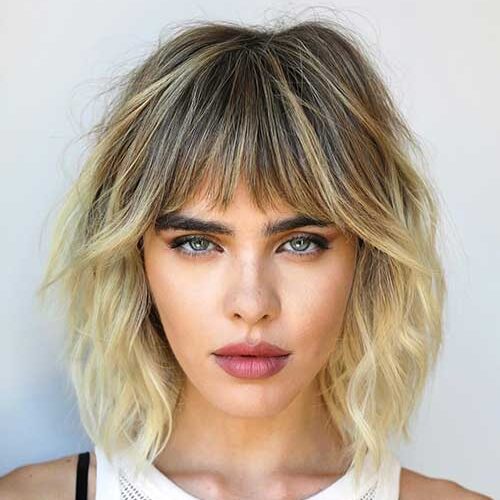A soft blonde short shag haircut with bangs and dark roots is one of the best short shag haircuts 2024