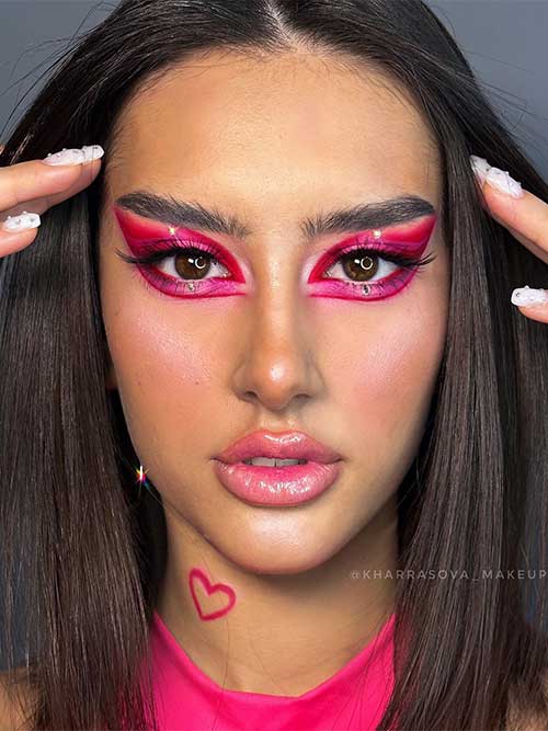 Creative red and hot pink winged Valentine's makeup look with glossy red lips and a hot pink heart shape on the neck