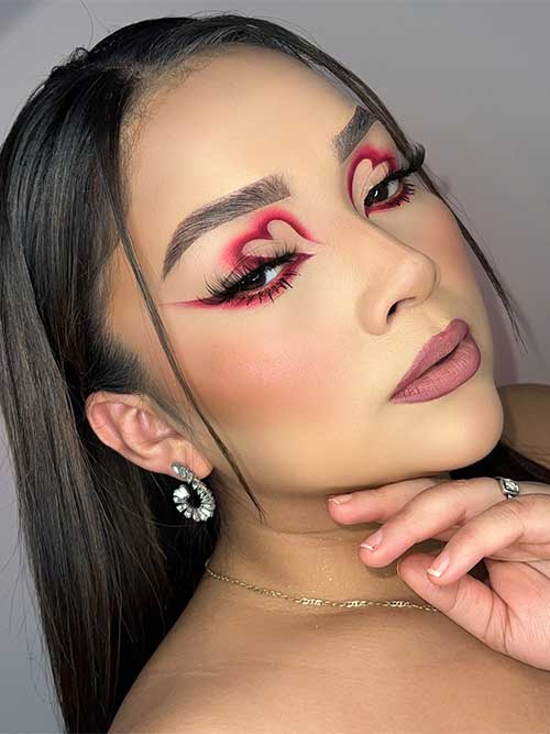 Creative red heart eyeshadow look with red-winged eyeliner, long lashes, and nude mauve lips