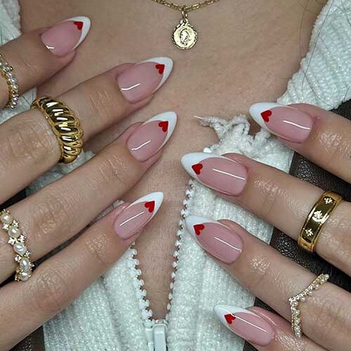 Cute almond-shaped white French Valentine's Day nails adorned with a red heart shape on the nail tip