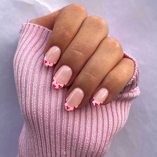 Cute short light pink French Valentine's Day nails adorned with tiny red heart shapes