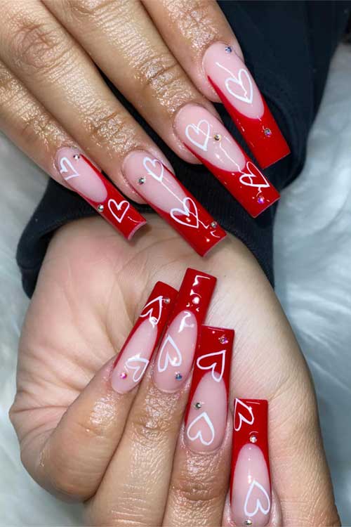 Long square red French Valentine's Day nails adorned with white hearts and sparkling rhinestones for a festive look.