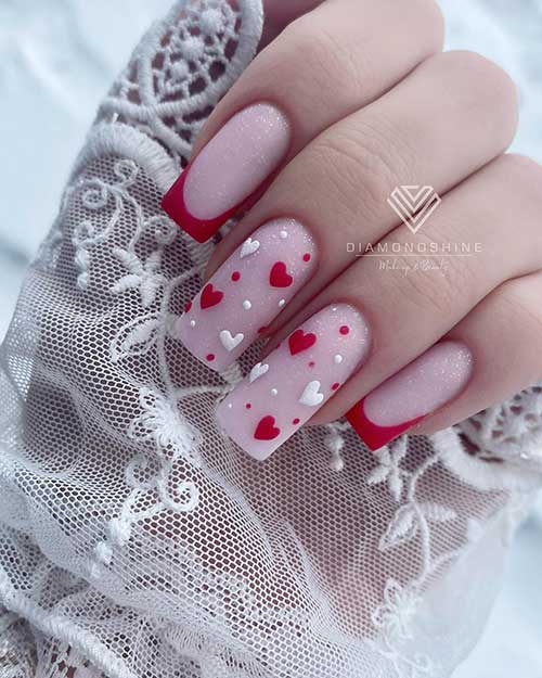 Red French Valentine's Day nails with gold glitter and two nude accent nails adorned with white and red hearts and dots