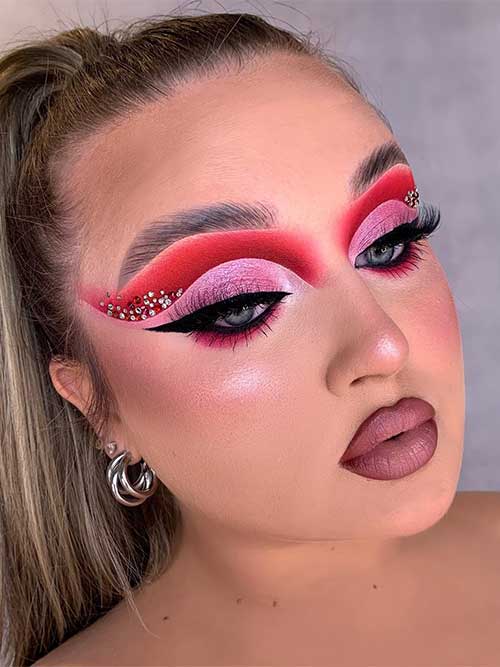 Red and pink winged eyeshadow look with red gems, black winged eyeliner, and matte nude mauve lips