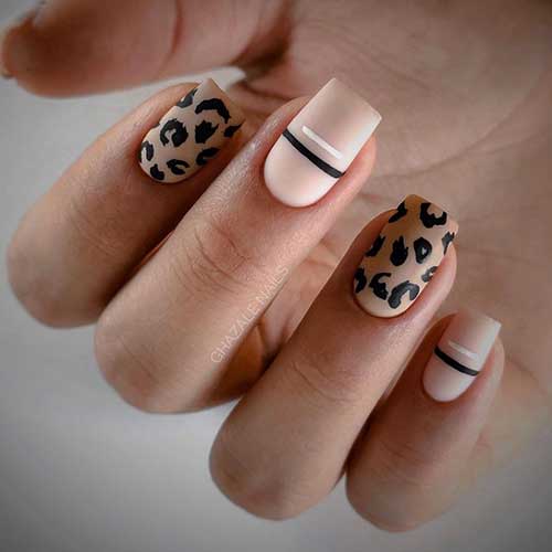 Short matte nude nails adorned with black and white lines on the nail center and two black leopard nails over a nude base