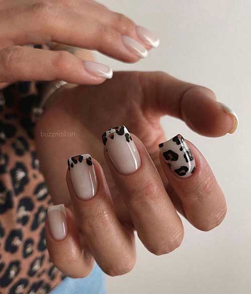 Short white French tip nails over nude base color and two accent French tips adorned with black and brown leopard prints