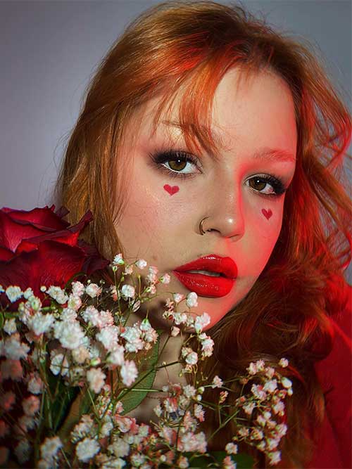 Simple and stunning Valentine’s makeup look using nude eyeshadow a red heart shape under each eye and glossy red lips