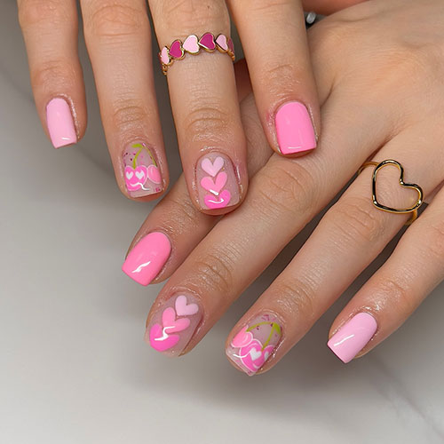 Cute short pink nails with two accent nude nails adorned with three different shades of pink heart shapes and heart fruits