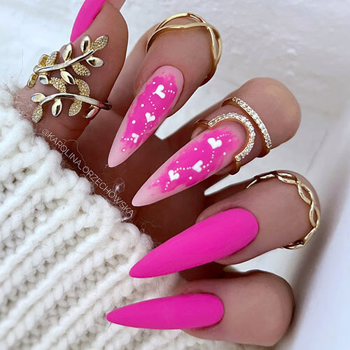 Gorgeous long stiletto-shaped matte pink Valentine’s Day nails with hot pink abstract nail art with white hearts and dots