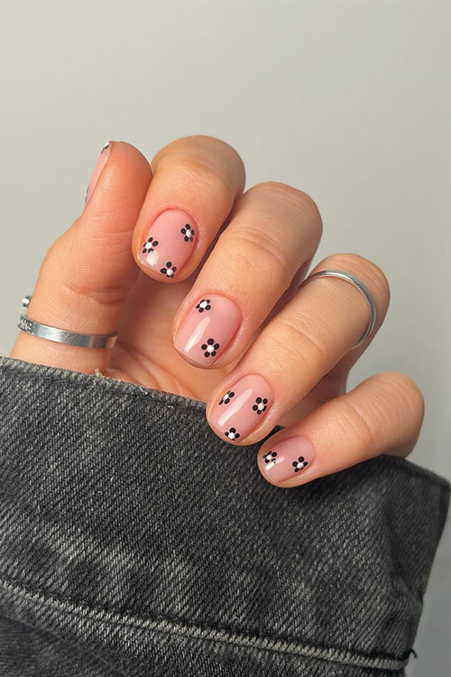 Chic short nude pink nails with tiny black flowers adorned with white color in their centers
