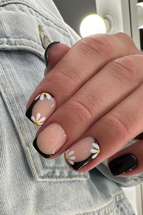 Glossy short black nails adorned with daisy flowers on two accent negative space nails and a black French tip accent nail