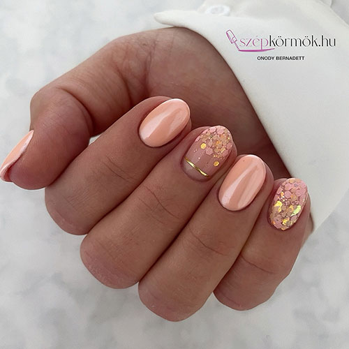 Short gel peach nails with two accent nude nails adorned with gold glam glitter and a stripe