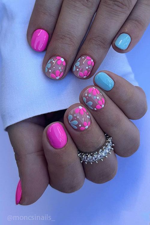 Short hot pink spring nails with an accent light blue nail and two accent nude nails adorned with pink and light blue flowers