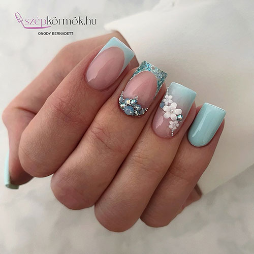 Sky blue nails with two French tip accents one of them adorned with glitter on the tip and rhinestones above the cuticle