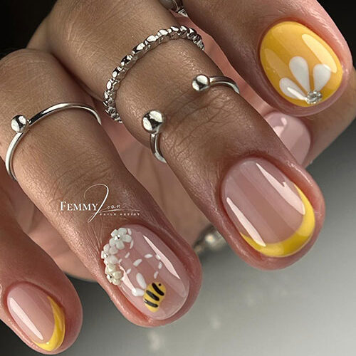 Yellow short spring nails feature two French accent nails and a nude accent nail adorned with bee and daisy flowers