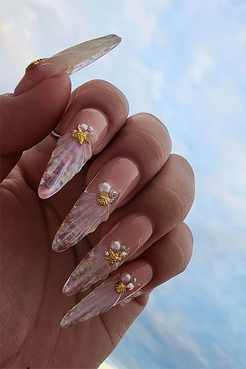 Long almond-shaped seashell nails on the nail tips and over a nude base color and adorned with seashell rhinestones