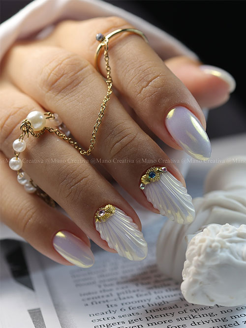 Medium almond-shaped white pearl chrome nails with two accent white seashell nails adorned with gold seashell rhinestones