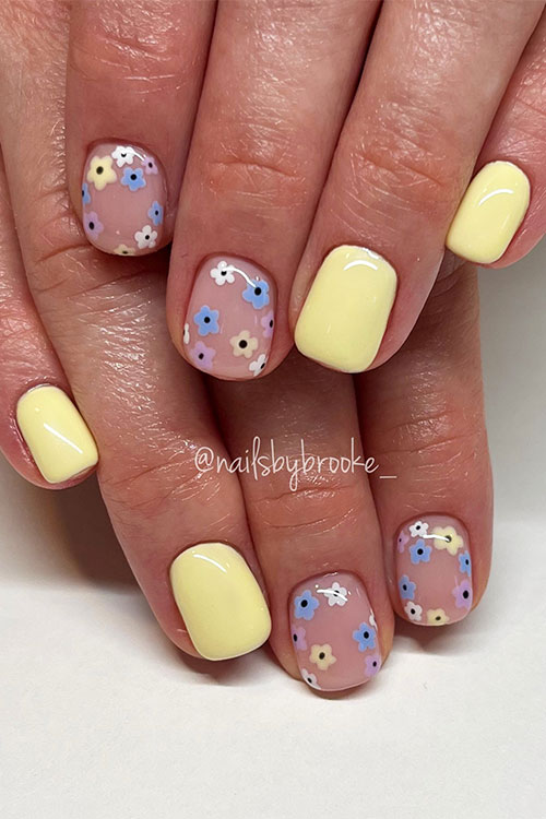 Short pastel yellow nails with two accent nude nails adorned with colorful tiny flowers