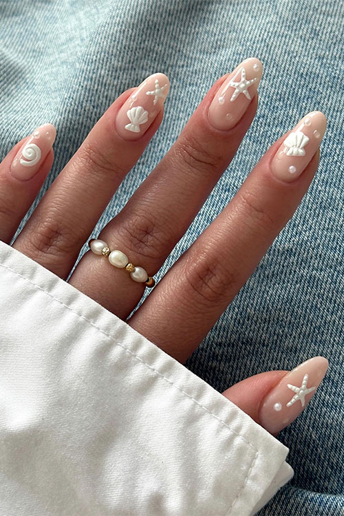 Simple nude almond nails adorned with seashells, sea stars, pearls, and sea snails