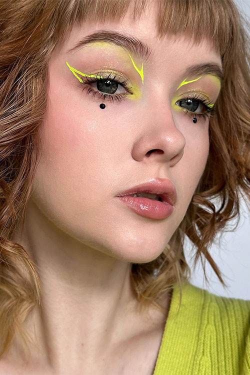 Vibrant neon yellow graphical eyeliner style with glossy nude lips