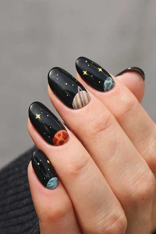 Creative black summer nails decorated with planets above the cuticles and a touch of yellow stars and dots