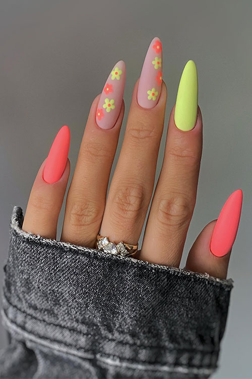 Long almond-shaped neon orange and yellow nails with two accent nude nails adorned with neon orange and yellow flowers