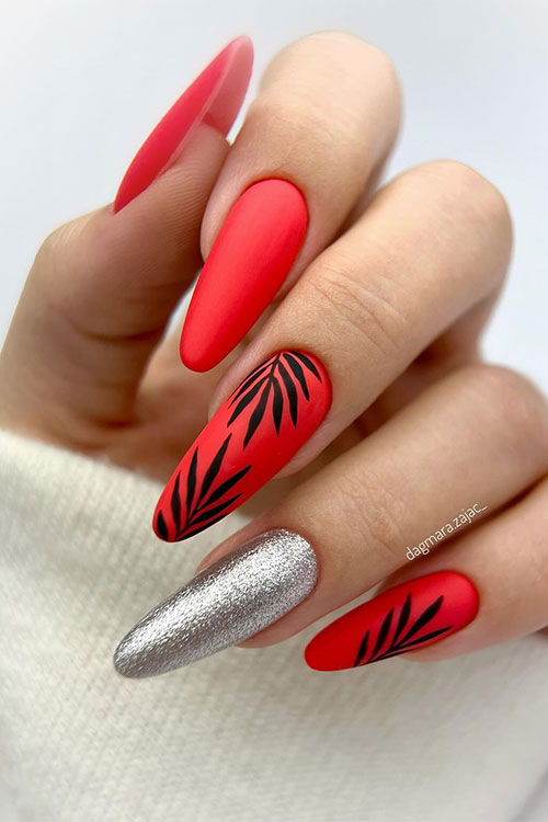 Long almond-shaped neon red matte nails with black leaves on two accent nails. Besides, a silver metallic accent nail