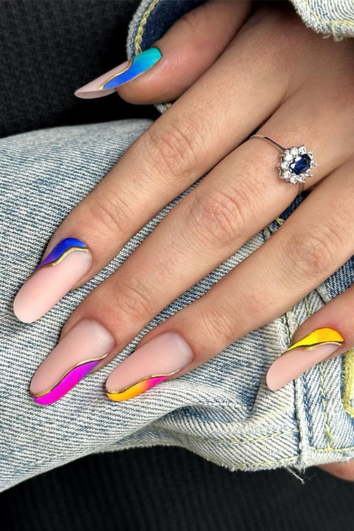 Long almond-shaped nude nails adorned with multicolored ombre diagonal nails with a twist feature black and gold swirls