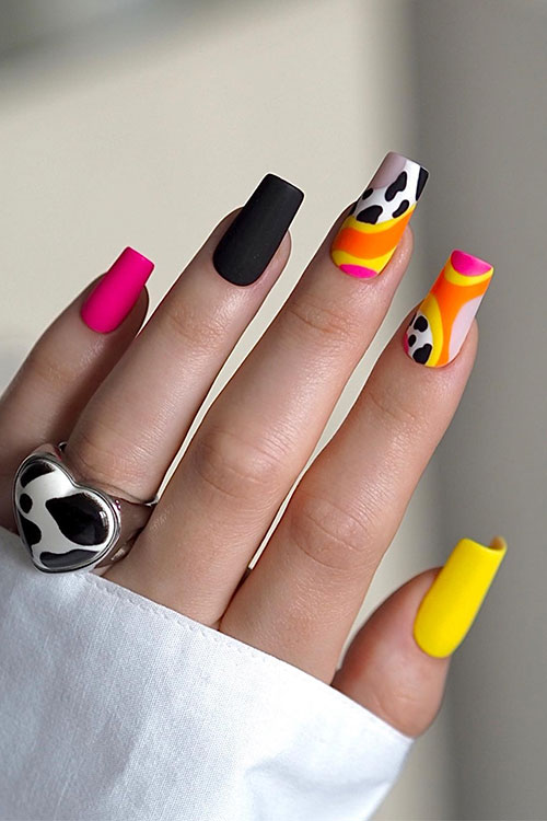 Matte pink, yellow, and orange neon nail design adorned with two accent nails feature abstract nail art and cow prints