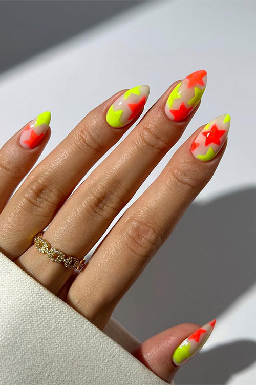 Medium-length orange and yellow star neon nails almond-shaped over a nude base color