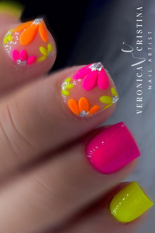 Short neon pink and yellow nails with two accent nude nails adorned with pink, yellow, and orange flowers