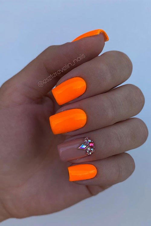 Simple short neon orange nails with a nude accent nail adorned with rhinestones above the cuticle area